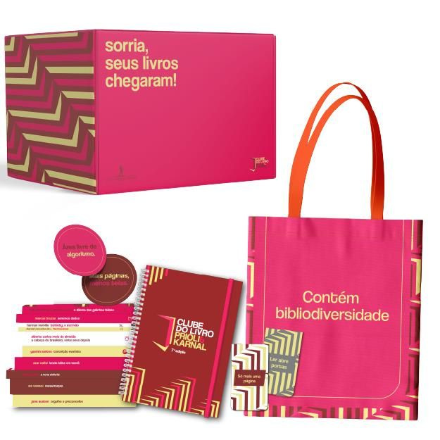 Flat‑lay do Box Clube do Livro 2026 com 10 livros de capa dura, sobrecapas exclusivas, planner, ecobag, caneca, marcador magnético e luminária, ambientado em mesa de madeira com luz natural.